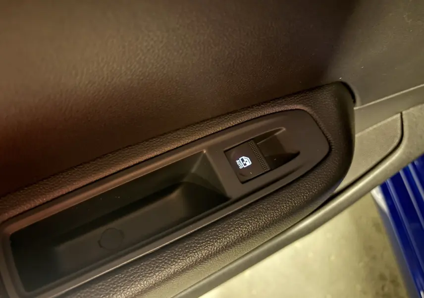 Gros plan sur le bouton de commande de la vitre électrique côté conducteur, avec partie de la porte bleu iron visible.