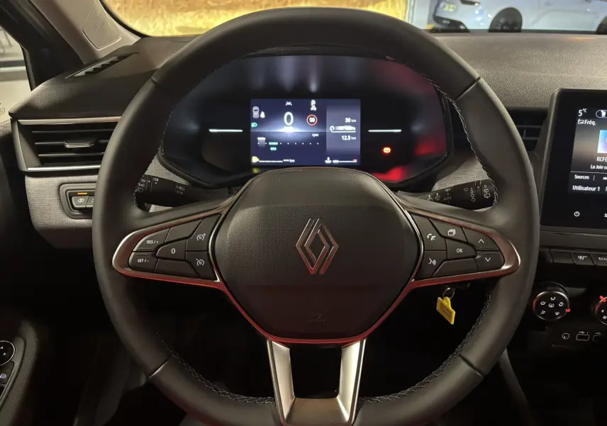 Vue intérieure centrée sur le volant de la Renault Clio 2024, avec tableau de bord numérique et commandes intégrées.