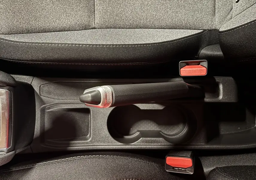 Vue plongeante sur le frein à main manuel et les porte-gobelets entre les sièges gris noir de la Renault Clio 2024.