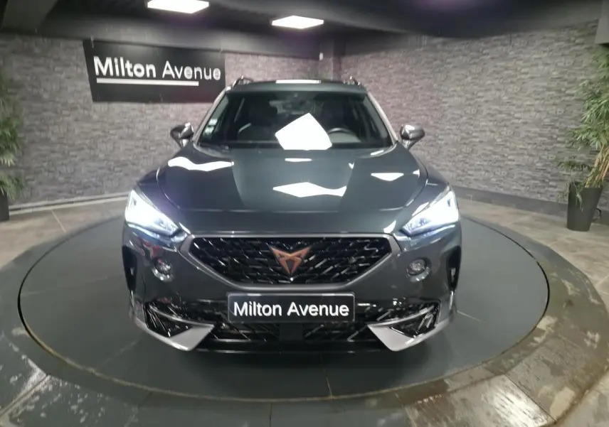 Vue de face du CUPRA Formentor gris avec calandre noire et éclairage LED allumé dans un showroom.