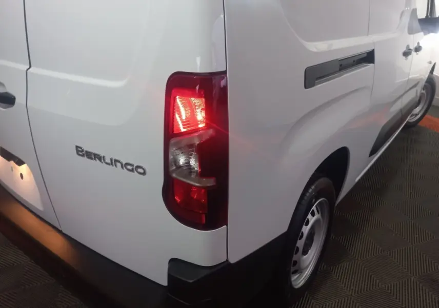 Vue arrière 3/4 droit d’un Citroën Berlingo blanc avec feu arrière allumé et logo Berlingo visible.