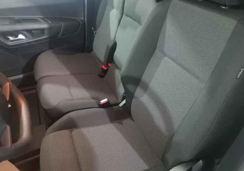Vue intérieure côté conducteur du Citroën Berlingo XL 2025, sièges tissu gris foncé avec ceinture rouge visible.