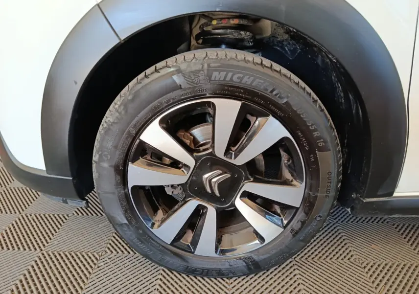 Gros plan sur la roue avant gauche blanche d'une Citroën C3 2021 avec jante alliage noire et argentée.