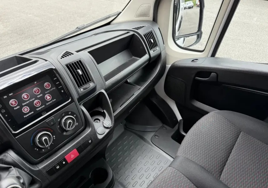 Vue intérieure côté passager du Peugeot Boxer Fourgon blanc 2023, montrant tableau de bord et siège tissu gris à motifs rouges.