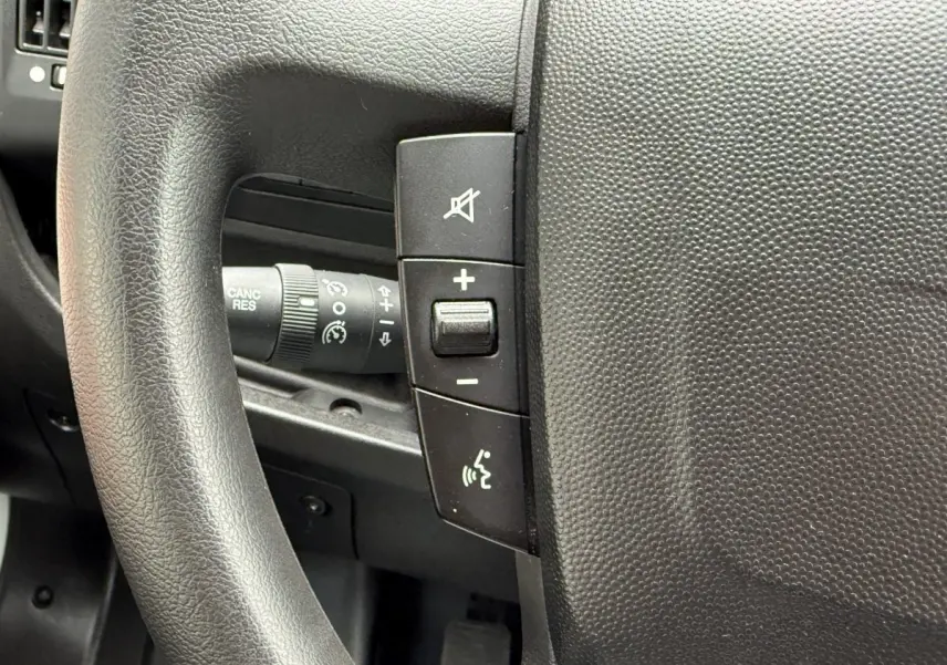 Gros plan sur le volant multifonctions noir du Peugeot Boxer Fourgon blanc, avec commandes de volume et régulateur.