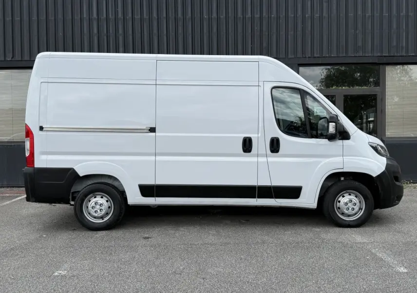 Vue de profil côté droit d’un Peugeot Boxer Fourgon blanc avec protections noires sur les bas de caisse et pare-chocs.