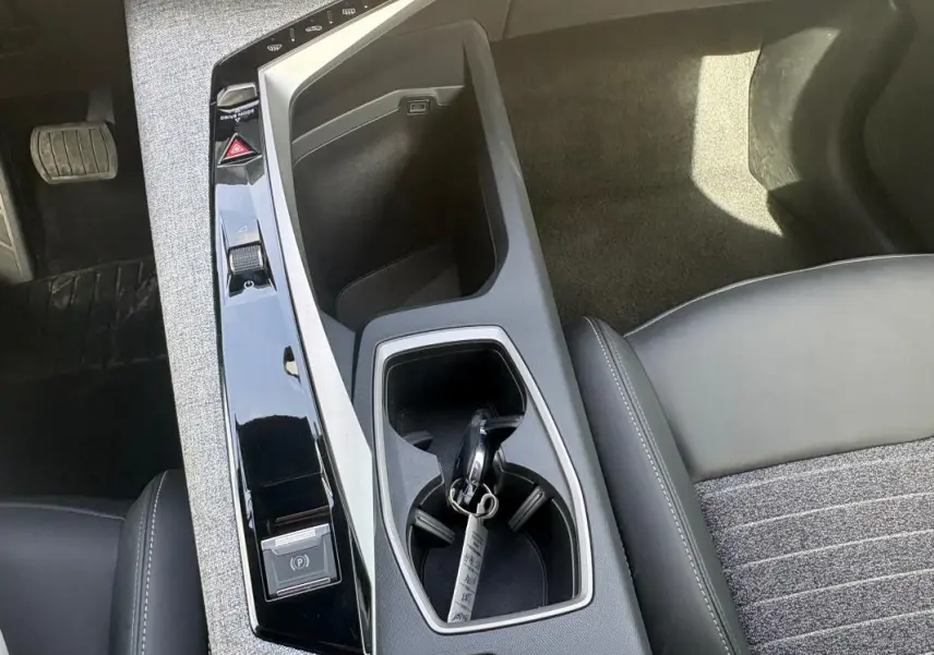 Vue plongeante sur la console centrale noire du Peugeot 3008 Hybrid 136 e-DCS6 Allure avec clé dans porte-gobelet.