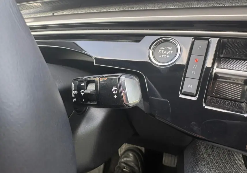 Gros plan sur la commande d’essuie-glace et le bouton start/stop du tableau de bord noir du Peugeot 3008 Hybrid 2025.