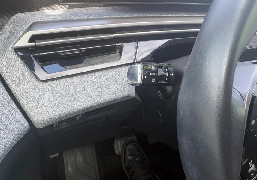Détail intérieur côté gauche du Peugeot 3008 Hybrid 2025, montrant la commande d’allumage automatique des feux et la finition tissu grise.