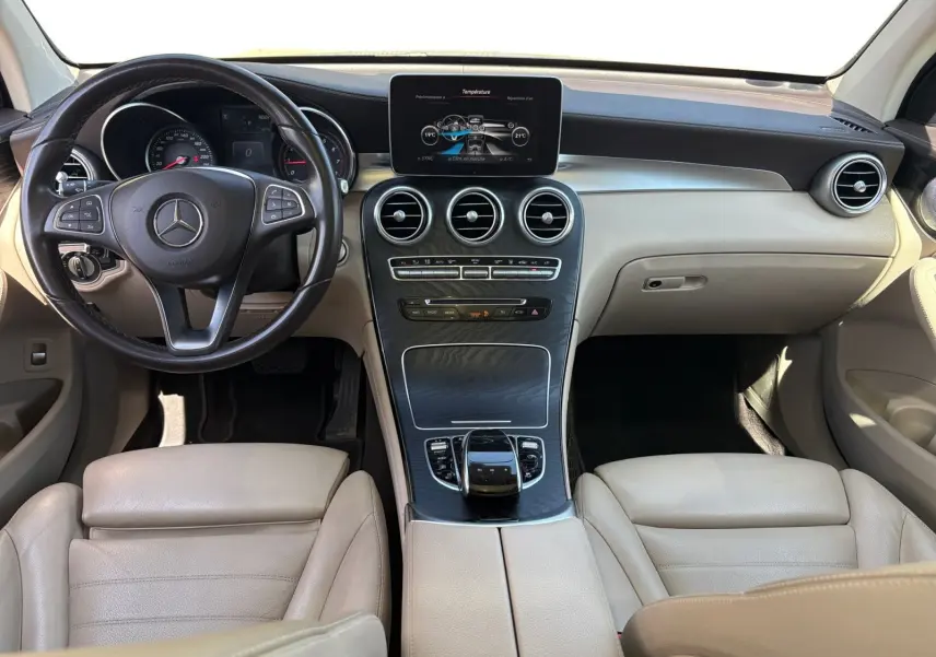 Vue intérieure frontale du tableau de bord beige et noir du Mercedes GLC 350 E Hybrid Fascination avec écran central et volant cuir.