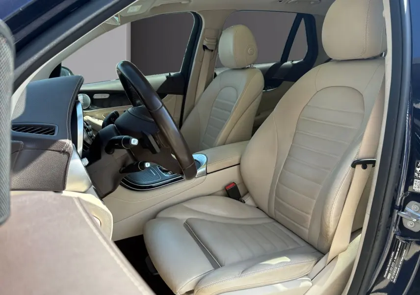 Vue intérieure côté conducteur d’un Mercedes GLC 350 E Hybrid Fascination bleu, avec sellerie cuir beige et volant noir.