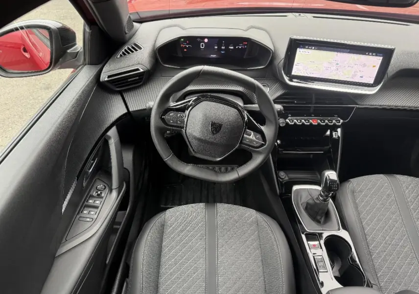 Vue intérieure centrée sur le volant et la console centrale d'une Peugeot 2008 rouge elexir, avec boîte manuelle et écran tactile.