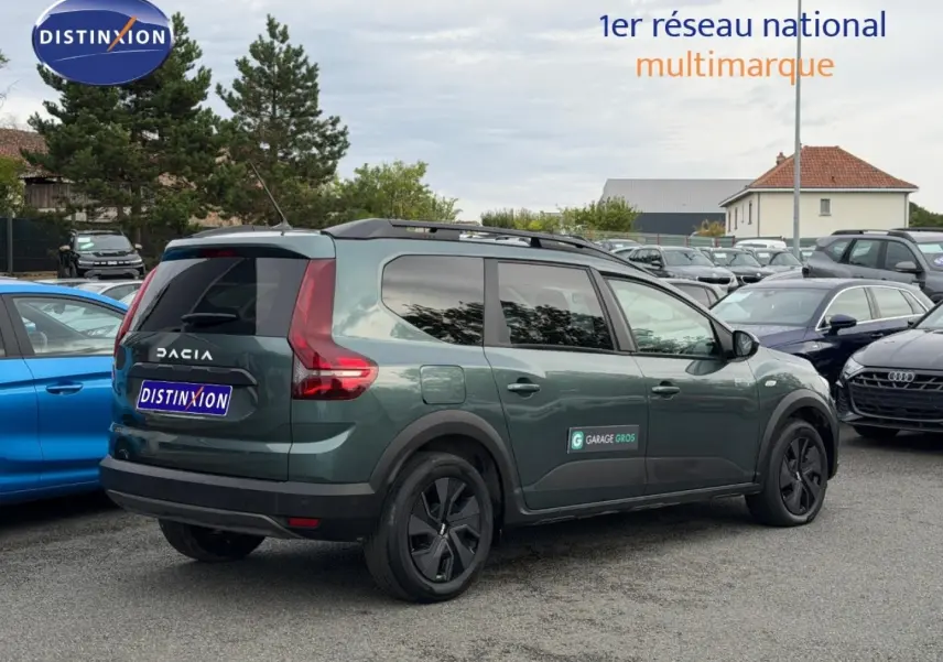Vue 3/4 arrière droite du Dacia Jogger 2025 vert cèdre métallisé avec barres de toit et vitres surteintées.