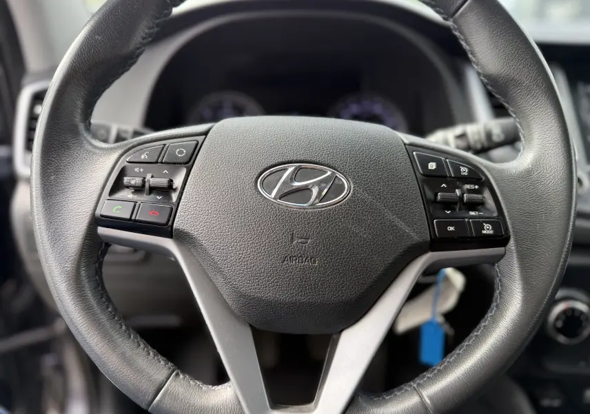 Gros plan sur le volant en cuir noir du Hyundai Tucson 2015 avec commandes intégrées et logo Hyundai central.