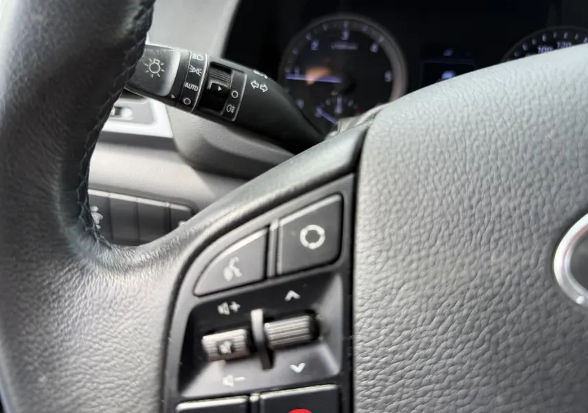 Gros plan sur le volant noir du Hyundai Tucson gris 2015, montrant les commandes audio et téléphone intégrées.