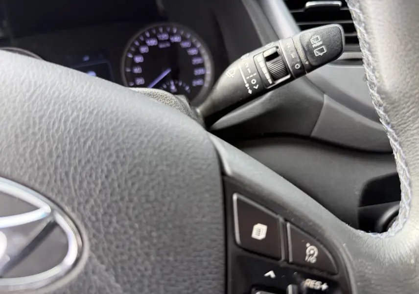 Gros plan sur le volant gris du Hyundai Tucson 2015 avec commandes au volant et manette d'essuie-glace visible.