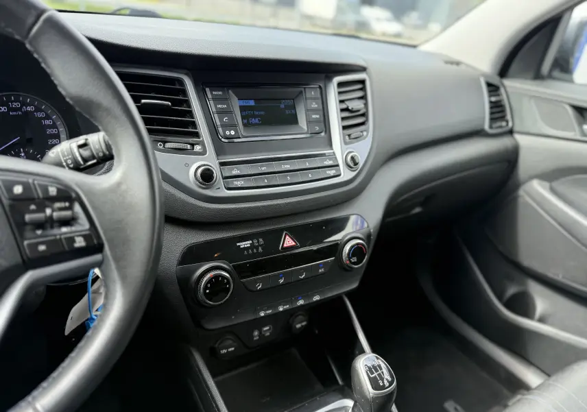 Intérieur du Hyundai Tucson 2015 gris, vue du tableau de bord côté conducteur avec console centrale et levier de vitesse manuel.