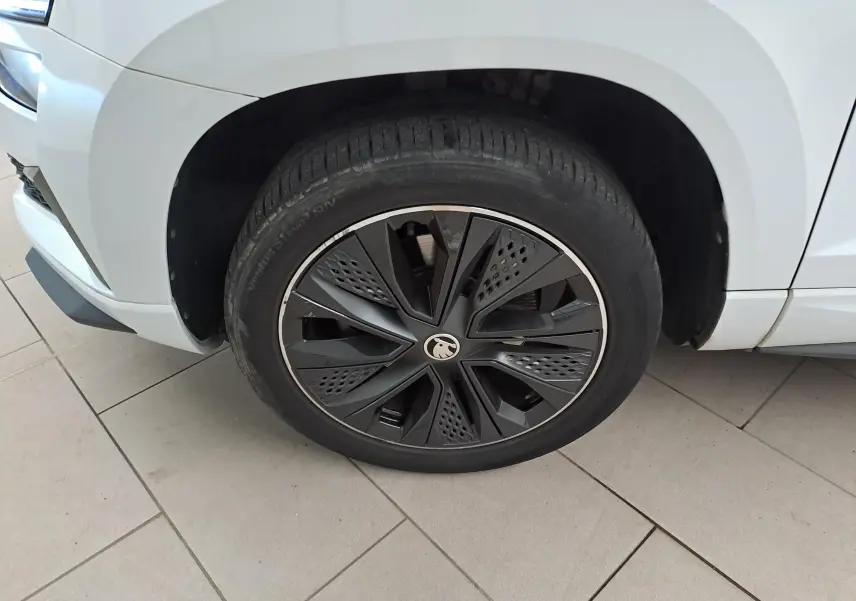 Gros plan sur la roue avant gauche du Skoda Karoq blanc Lune, mettant en valeur la jante noire au design moderne.