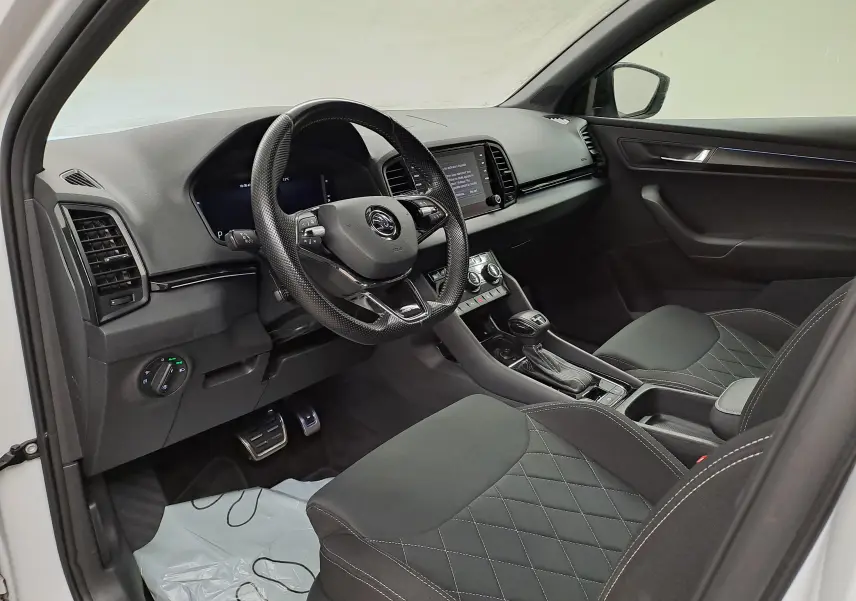 Vue intérieure côté conducteur du Skoda Karoq 2022, mettant en valeur le volant multifonction et les sièges noirs à surpiqûres.