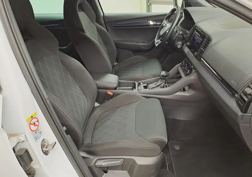 Vue intérieure côté conducteur du Skoda Karoq 2022 blanc lune, sièges sport noirs avec surpiqûres grises et console centrale visible.