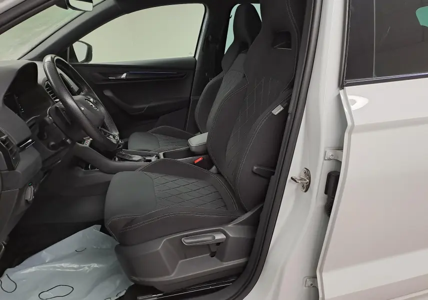 Vue intérieure côté conducteur du Skoda Karoq blanc Lune 2022, mettant en valeur les sièges sport noirs avec surpiqûres.