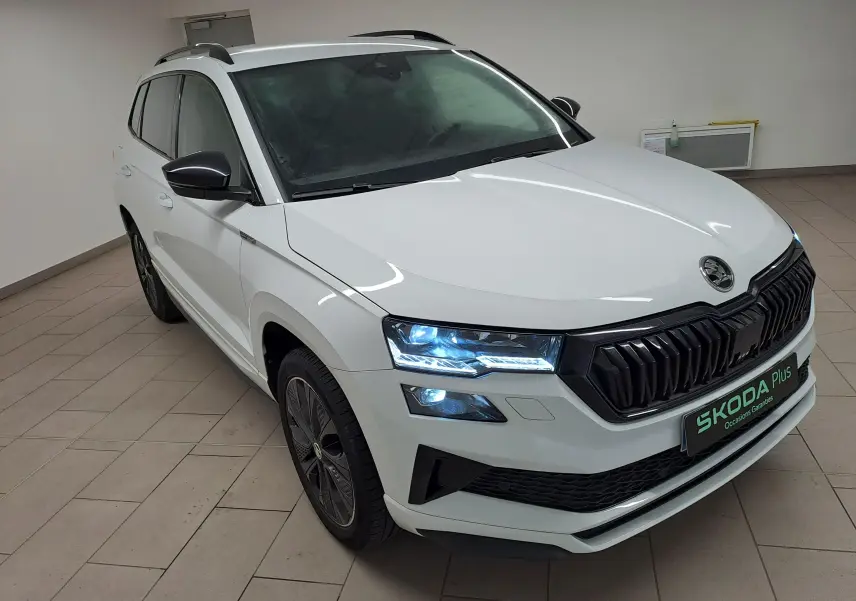 Vue 3/4 avant droite du Skoda Karoq blanc lune 2022 avec calandre noire et feux LED allumés en intérieur.