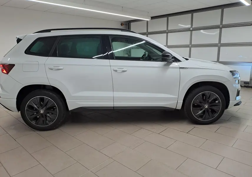 Vue de profil côté gauche d'un Skoda Karoq 2.0 TDI 116 DSG7 Sportline blanc lune avec jantes noires distinctives.