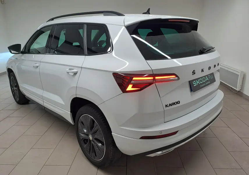 Vue 3/4 arrière droite du Skoda Karoq blanc lune 2022 avec feux allumés et jantes noires sportline.