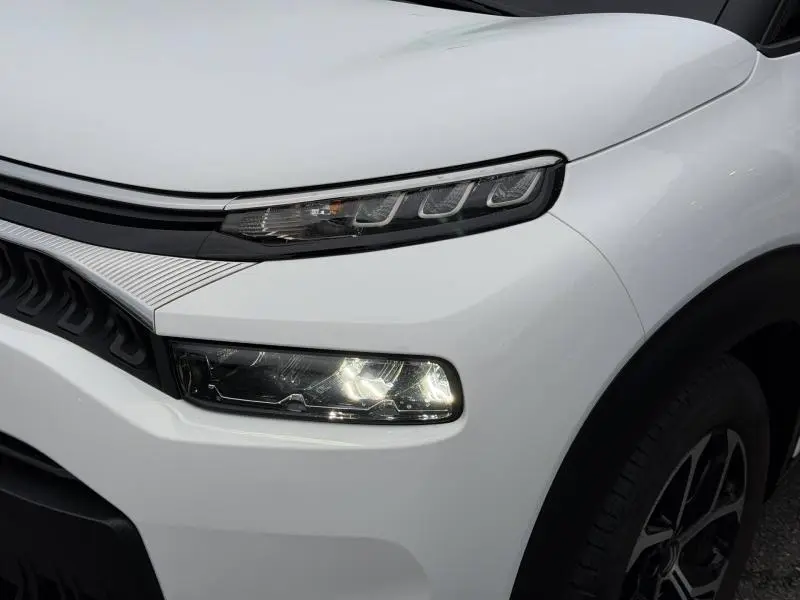 Gros plan sur l'avant droit blanc Banquise du Citroën C3 Aircross 2024 avec phares LED allumés et jante alu visible.