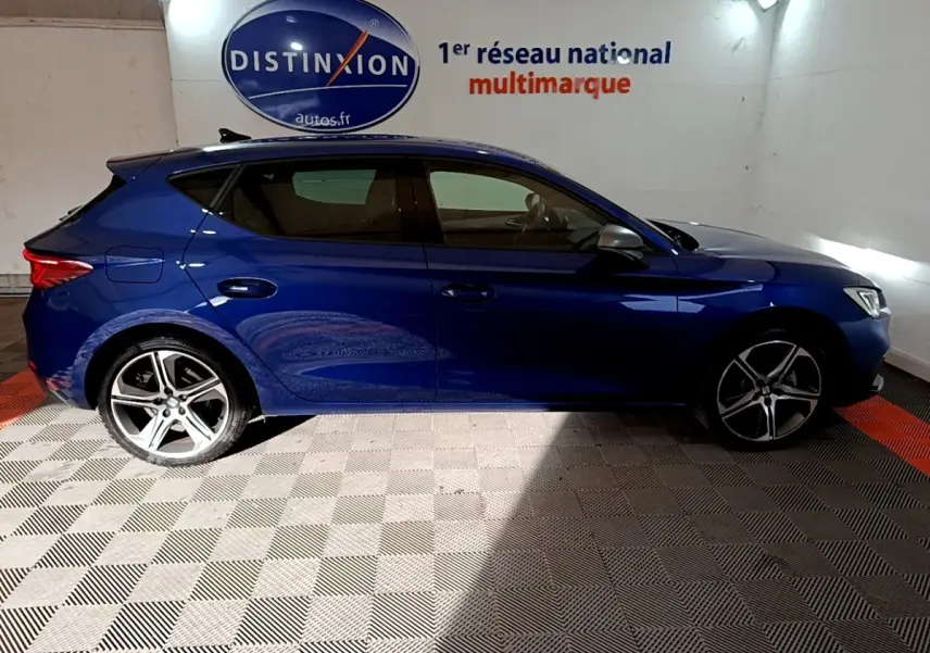 Vue de profil côté gauche d'une SEAT Leon bleu 2021 dans un showroom avec jantes alliage et vitres teintées.