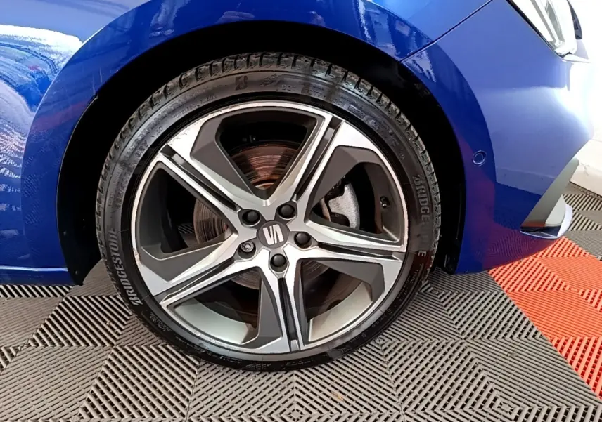 Gros plan sur la roue avant gauche d’une SEAT Leon bleu 2021 avec jante alliage à cinq branches.