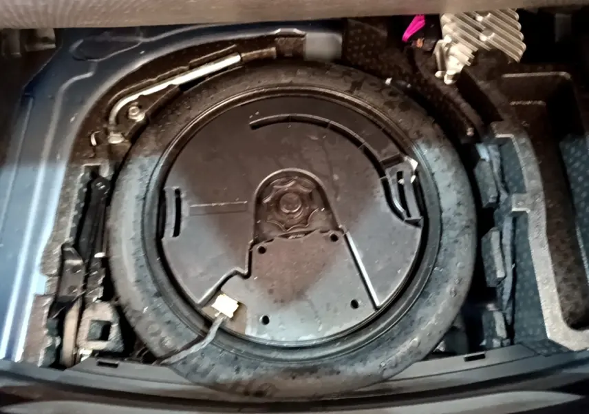 Vue en plongée sur la roue de secours et le kit de réparation dans le coffre d'une SEAT Leon 1.5 eTSI bleu 2021.