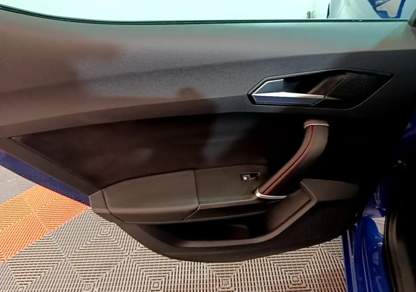 Intérieur côté gauche de la porte avant d’une SEAT Leon bleu, avec poignée noire et surpiqûres rouges.