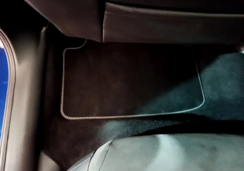 Vue intérieure du plancher côté passager arrière d'un SEAT Leon bleu, avec tapis de sol noir et couture claire visible.