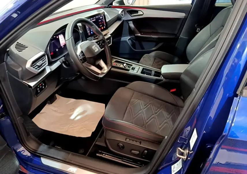 Vue intérieure côté conducteur d’une SEAT Leon bleu 2021, avec sièges noirs et tableau de bord digital lumineux.