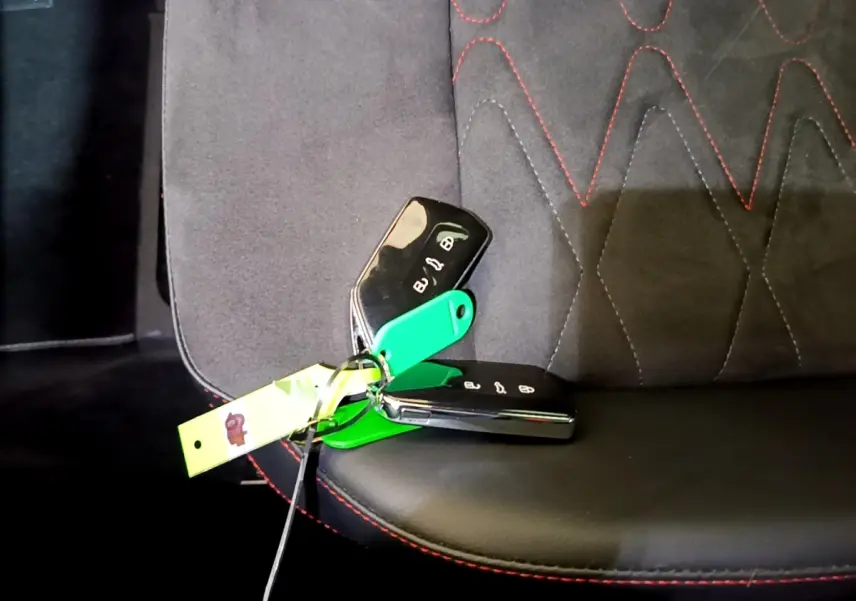 Gros plan sur les clés de voiture SEAT Leon posées sur un siège tissu noir avec surpiqûres rouges.