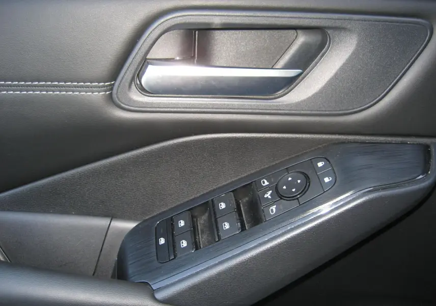 Gros plan sur la commande de lève-vitres et la poignée intérieure côté conducteur du Nissan Qashqai blanc nacré 2024.