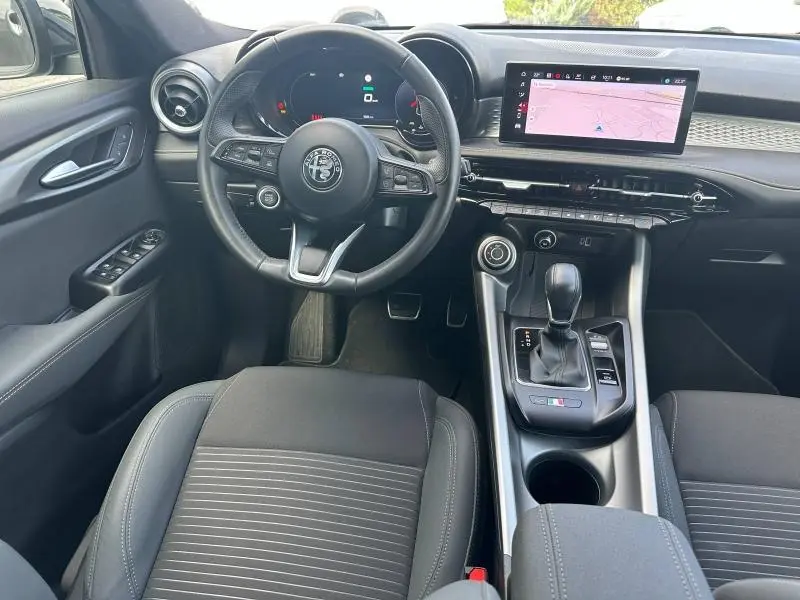 Vue intérieure avant de l'Alfa Romeo Tonale 1.5 Hybrid avec volant cuir, écran tactile GPS et console centrale noire.