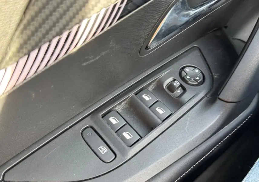 Gros plan sur les commandes des vitres électriques et rétroviseurs sur la porte côté conducteur du Peugeot 2008 noir.