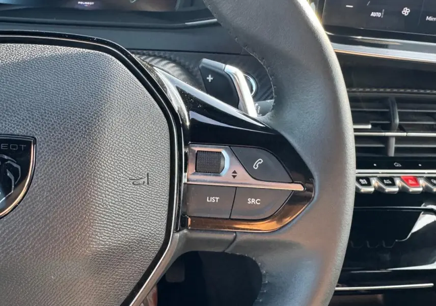 Gros plan sur le volant noir du Peugeot 2008 Hybrid 136 Allure 2025, avec commandes intégrées et tableau de bord partiel visible.
