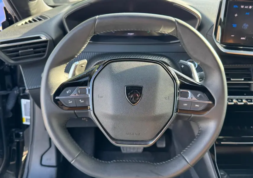 Vue rapprochée du volant noir de la Peugeot 2008 Hybrid 136 e-DCS6 Allure avec commandes intégrées.