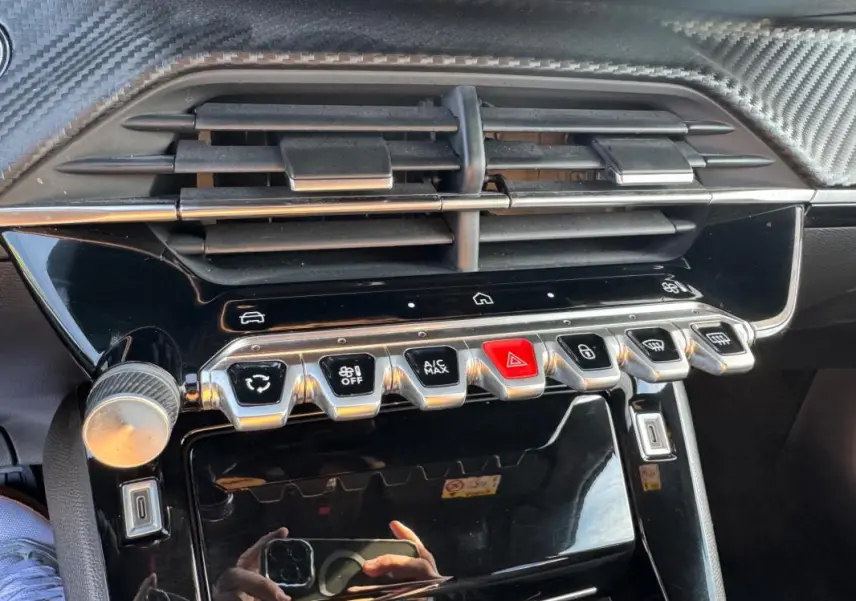 Gros plan sur la console centrale noire du Peugeot 2008 Hybrid 136, avec boutons de commande et aérateurs.
