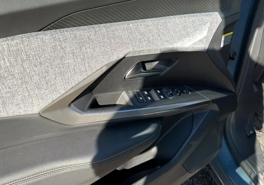 Détail de la porte avant gauche du Peugeot 3008 bleu 2025, avec commandes de vitres et habillage tissu gris.
