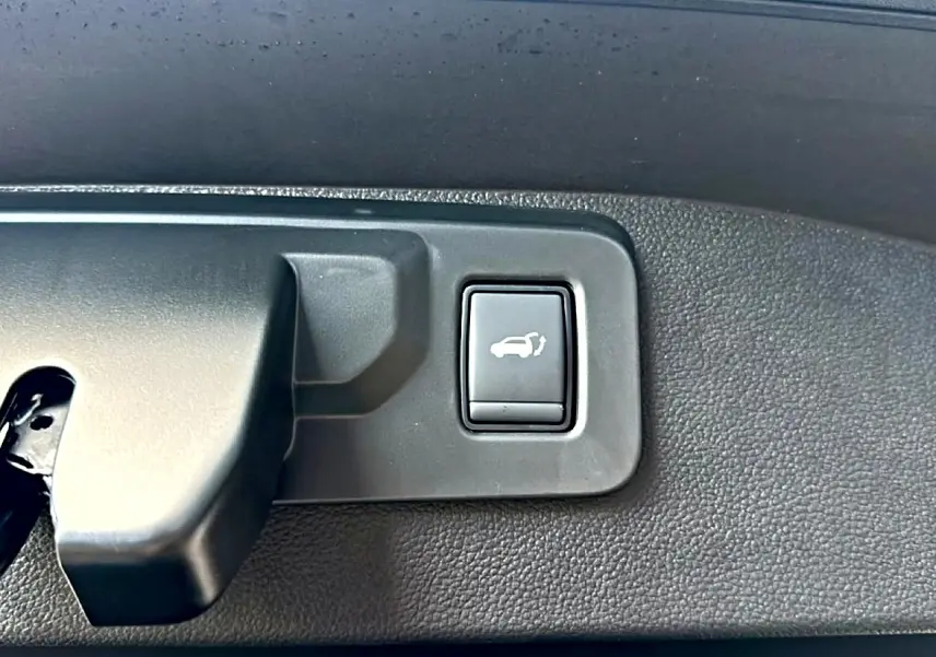 Gros plan sur le bouton d'ouverture électrique du hayon dans le coffre du Renault Austral bleu outremer 2026.