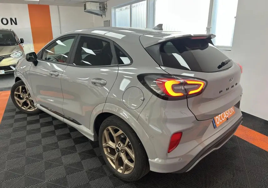 Ford Puma gris métallisé vu de l'arrière droit avec jantes alliage dorées et feux arrière LED allumés.