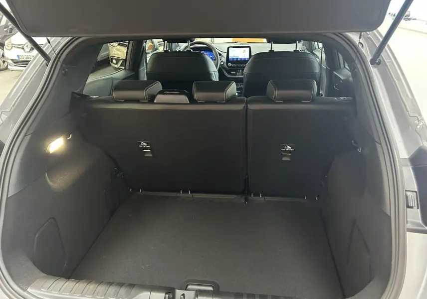 Coffre ouvert d'un Ford Puma gris 3/4 arrière, montrant l'espace de chargement et les sièges arrière noirs.
