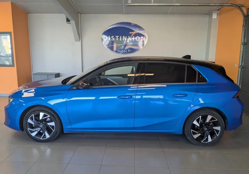 Profil latéral droit d'une Opel Astra 2022 bleu vif avec toit noir et jantes alliage bicolores dans un showroom.