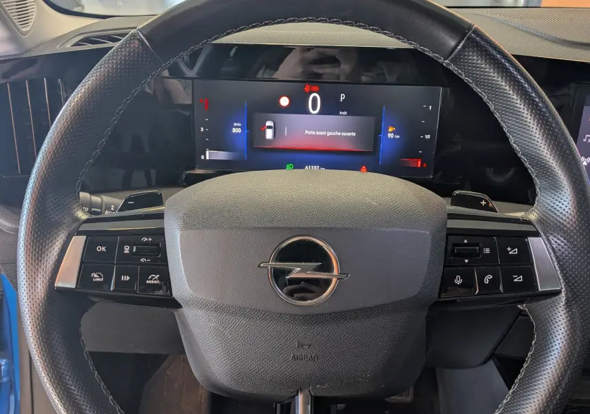 Vue intérieure centrée sur le volant noir perforé et le tableau de bord numérique de l'Opel Astra bleu 2022.