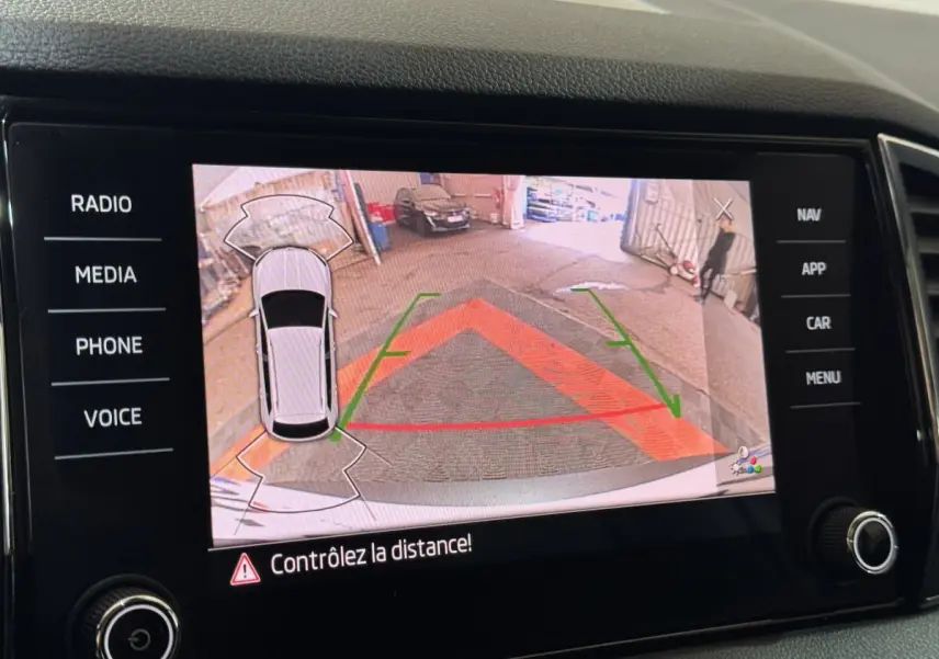 Écran tactile affichant la caméra de recul du Skoda Karoq blanc, avec repères de stationnement colorés.
