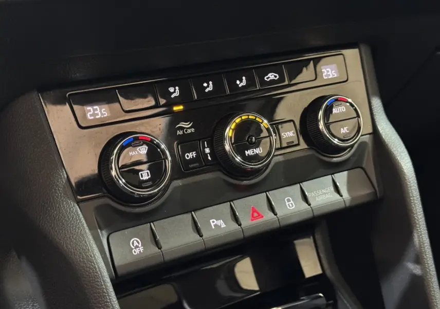 Gros plan sur la console centrale noire du SKODA KAROQ blanc 2021, montrant les commandes de climatisation digitale et boutons fonctionnels.